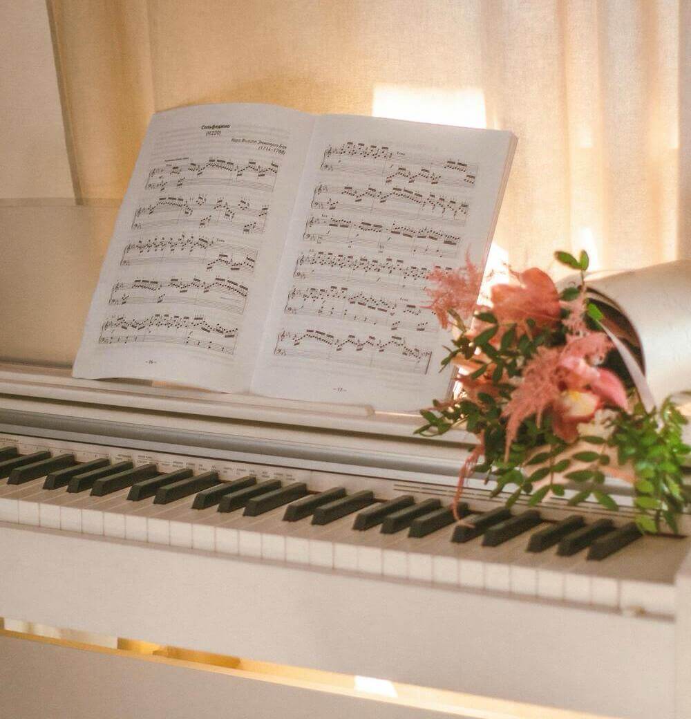 A piano with an open music sheet and a floral arrangement on the side